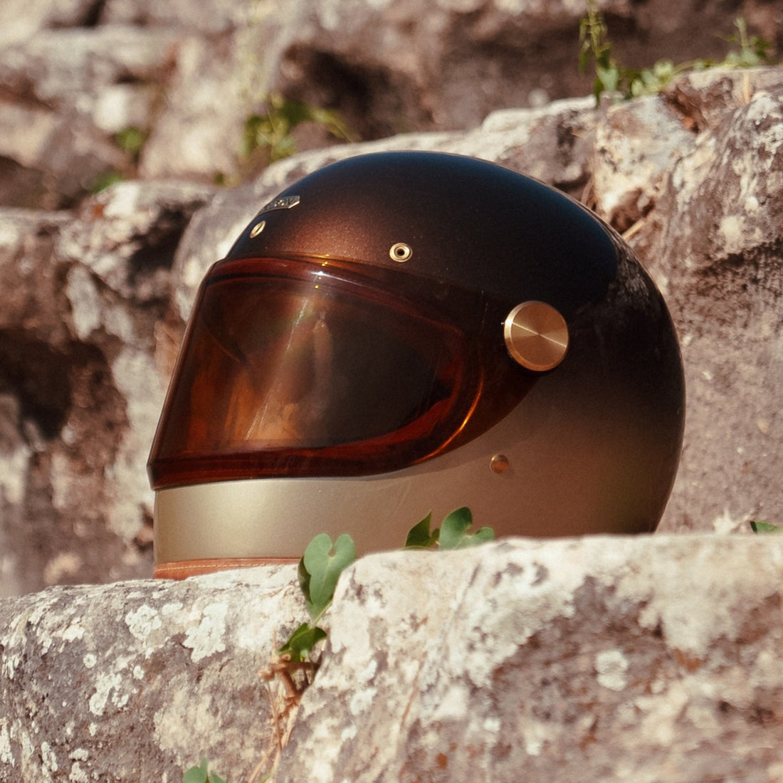 Full-face motorcycle helmet with a brown and beige gradient paint finish, placed on a rocky surface.