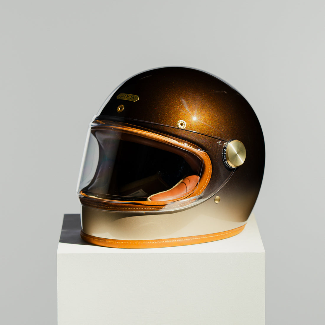 Brown motorcycle helmet on a white stand with a gray background