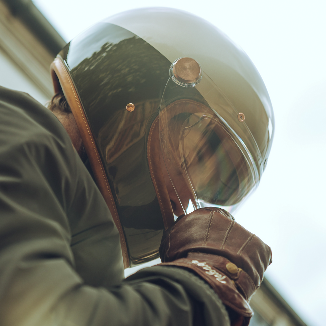 A person wearing a full-face motorcycle helmet with a metallic finish and leather details. The helmet features a visor and is designed for comfort and style.