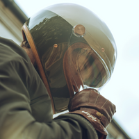 A person wearing a full-face motorcycle helmet with a metallic finish and leather details. The helmet features a visor and is designed for comfort and style.